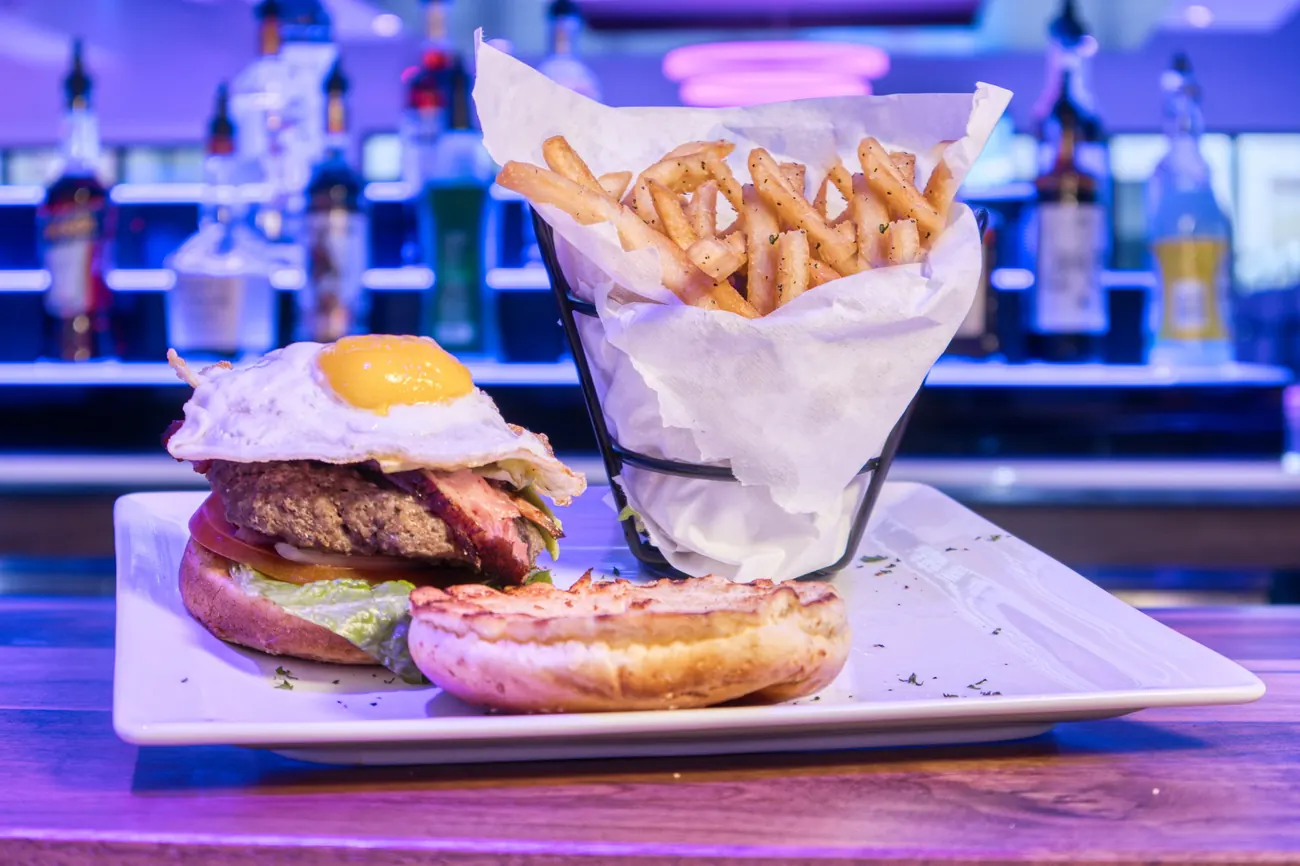 Burger topped with a fried egg, with seasoned fries at the bar